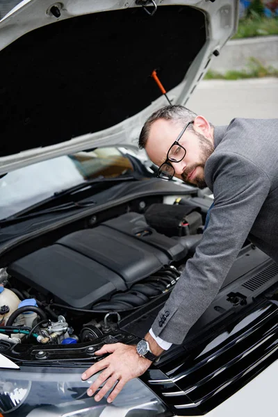 Bel homme d'affaires appuyé sur le capot ouvert de voiture et regardant la caméra — Photo de stock