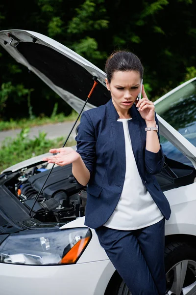 Arrabbiato donna d'affari parlando da smartphone vicino rotto auto — Foto stock