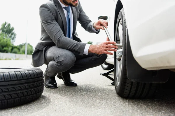Обрезанный образ бизнесмена, меняющего шины на автомобиле на дороге — стоковое фото