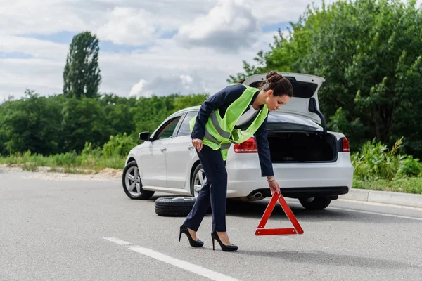 Atractiva mujer de negocios en chaleco verde claro poner señal de stop en la carretera cerca de coche roto - foto de stock