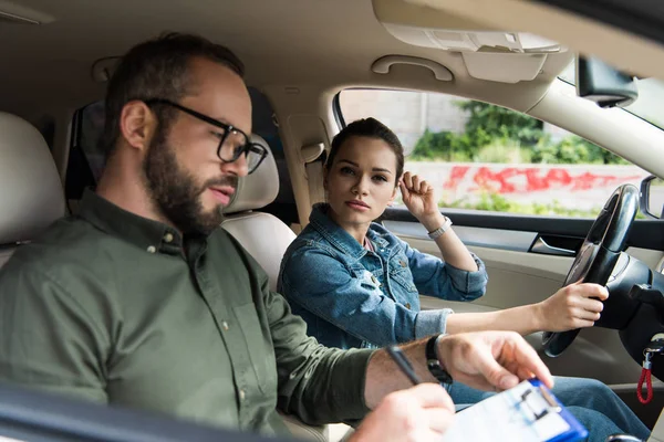 Female student and male teacher in car during driving test — Stock Photo