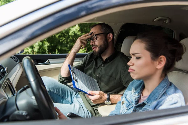 Dissatisfied teacher touching forehead in car during driving test — Stock Photo