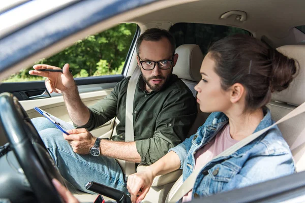 Profesor señalando algo al estudiante en el coche durante el examen de conducir - foto de stock