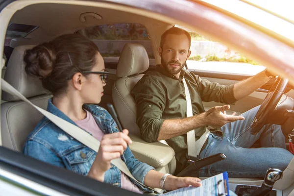 Estudiante y profesor mirándose el uno al otro en coche en el examen de conducir - foto de stock