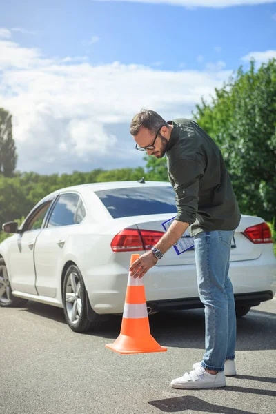 Bel homme tenant une assurance auto et mettant des cônes de sécurité sur la route — Photo de stock