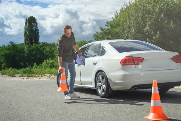 Bell'uomo che tiene l'assicurazione auto e mette i coni del traffico sulla strada — Foto stock