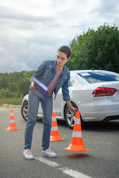 Attraente donna in possesso di assicurazione auto e mettere i coni del traffico su strada — Foto stock