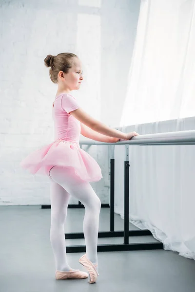 Vue latérale de l'adorable petite ballerine en tutu rose s'exerçant à l'école de ballet — Photo de stock