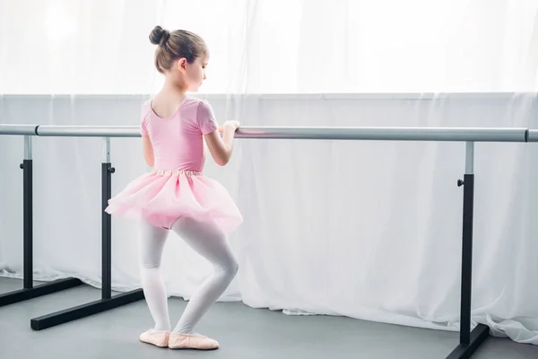 Vista posterior de un niño pequeño en tutú rosa practicando ballet en la escuela de ballet - foto de stock