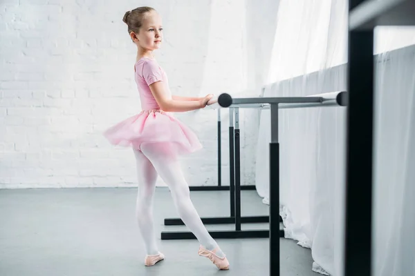 Vista lateral de la adorable bailarina en tutú rosa practicando ballet y mirando hacia otro lado — Stock Photo