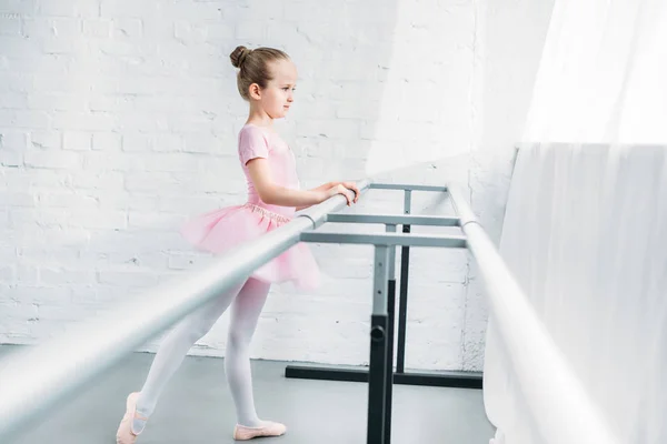 Side view of graceful little ballerina in pink tutu exercising in ballet school — Stock Photo