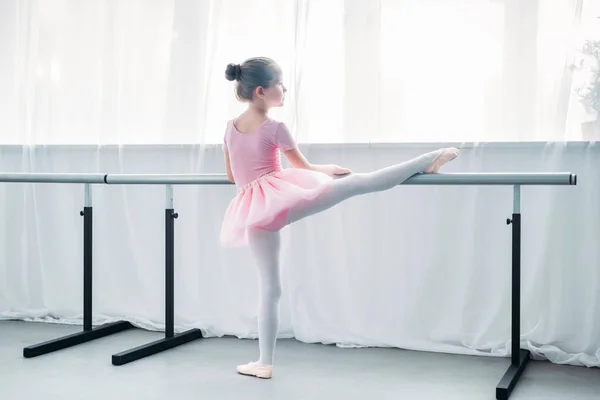 Vista posterior de un niño pequeño en tutú rosa haciendo ejercicio en la escuela de ballet - foto de stock