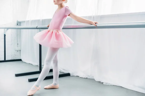 Обрезанный снимок очаровательной маленькой балерины в розовой пачке, практикующейся в балетной студии — стоковое фото