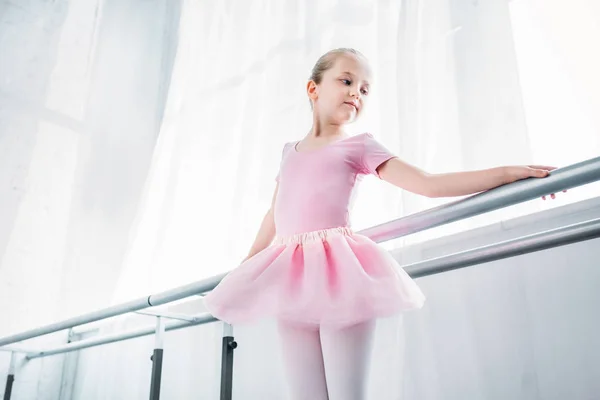 Vue en angle bas d'adorable enfant en tutu rose pratiquant en studio de ballet — Photo de stock