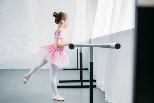 Vue latérale de l'enfant en tutu rose pratiquant le ballet en studio — Photo de stock
