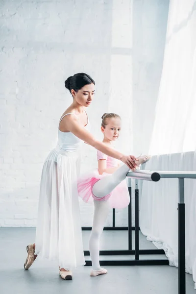 Criança adorável em tutu rosa alongamento enquanto pratica balé com professor — Fotografia de Stock