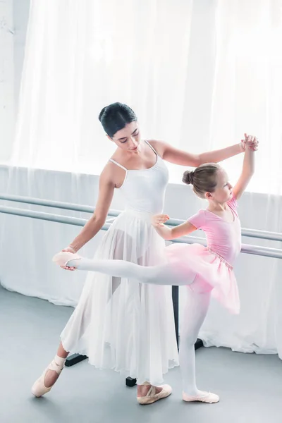 Vue grand angle d'adorable enfant en tutu rose pratiquant le ballet avec jeune professeur à l'école de ballet — Photo de stock