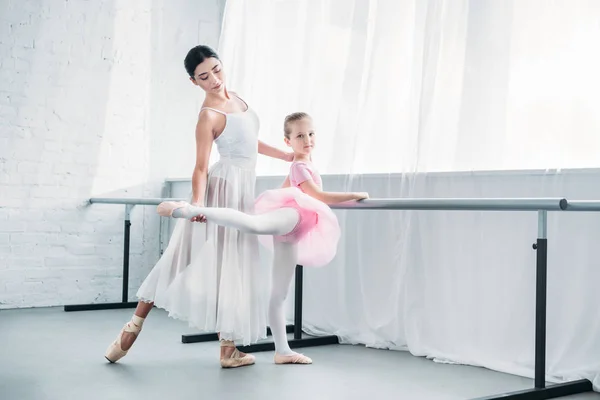 Hermoso niño en tutú rosa practicando ballet con joven profesor en estudio de ballet - foto de stock