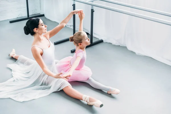 Vista de ángulo alto de un niño adorable en tutú rosa haciendo ejercicio con el profesor en la escuela de ballet - foto de stock