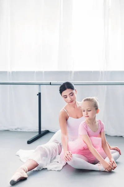 Красивая молодая балерина смотрит на ребенка в розовой пачке, занимающегося в балетной школе — стоковое фото