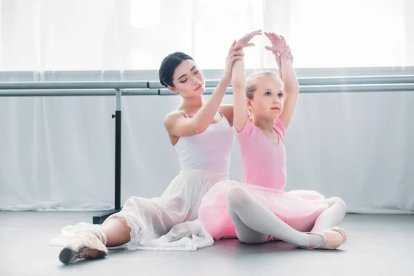 Bailarina adulta haciendo ejercicio con un lindo niño pequeño en tutú rosa en la escuela de ballet - foto de stock