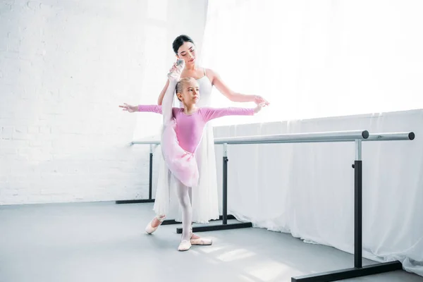 Adorable little ballerina in pink tutu exercising with teacher in ballet school — Stock Photo