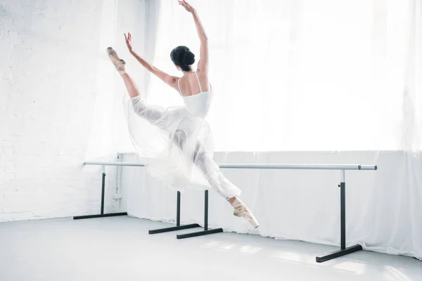 Vista trasera de la elegante bailarina joven en vestido blanco bailando en el estudio de ballet - foto de stock