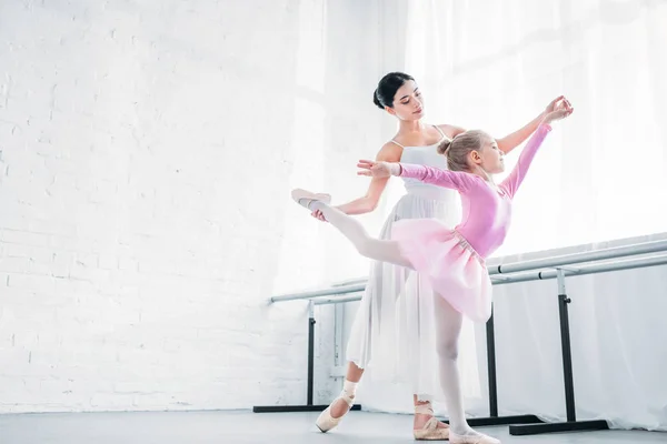 Low angle view of adult ballerina training with child in pink tutu in ballet studio — Stock Photo