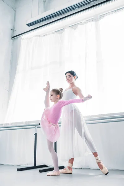 Visión de bajo ángulo de la formación de maestros de ballet jóvenes con estiramiento infantil en la escuela de ballet - foto de stock