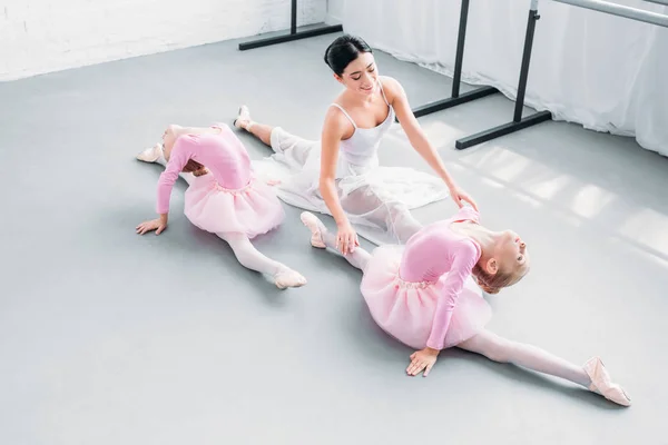 Vista de ángulo alto del joven profesor sonriente con lindas bailarinas haciendo ejercicio en la escuela de ballet - foto de stock