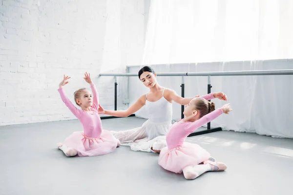 Учитель балета с детьми в юбочках, сидящими и растянутыми в балетной школе — стоковое фото