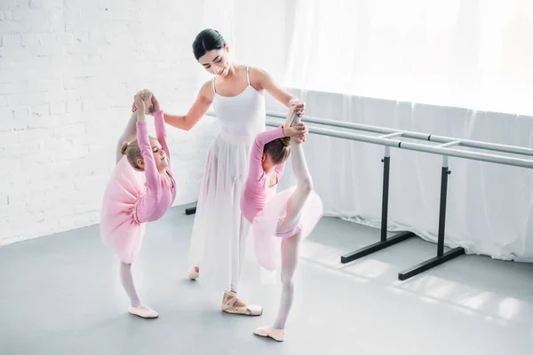 Smiling young ballet teacher exercising with kids in ballet school — Stock Photo