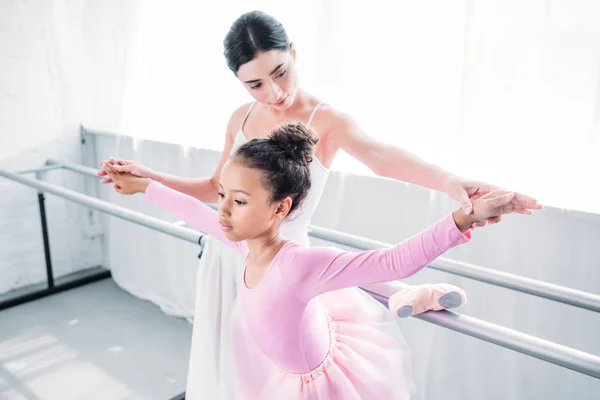 Lindo africano americano niño en rosa tutú ejercicio con profesor en ballet escuela - foto de stock