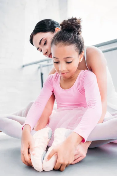 Cute african american child in pink tutu stretching while training with teacher in ballet school — Stock Photo