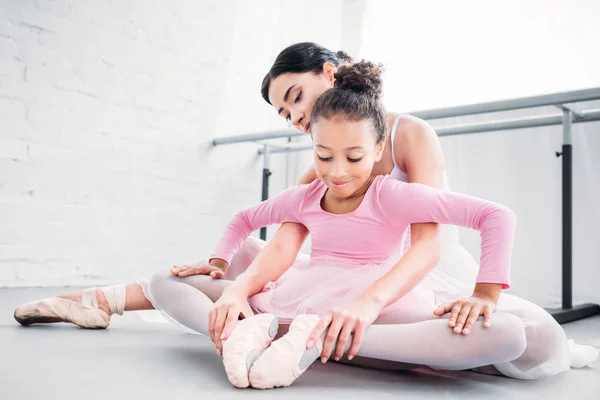 Enfant afro-américain souriant en tutu rose s'étirant tout en s'entraînant avec le professeur à l'école de ballet — Photo de stock