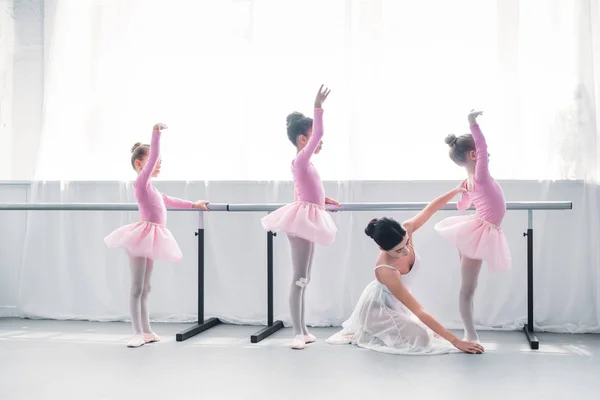 Vista lateral del joven profesor de ballet haciendo ejercicio con niños en la escuela de ballet - foto de stock