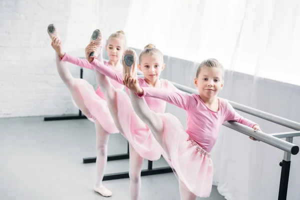 Очаровательные дети в розовых юбочках в балетной пачке, практикующие балет и смотрящие в камеру в балетной школе — стоковое фото