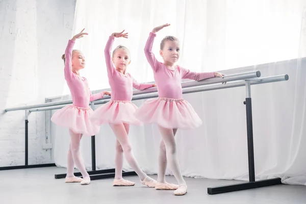 Vista completa de adorables niños pequeños en faldas tutú rosadas bailando en estudio de ballet - foto de stock