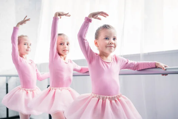 Adorables niños sonrientes en faldas de tutú rosa bailando en estudio de ballet - foto de stock