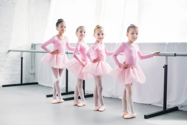 Niedliche multiethnische Kinder in rosa Tutu-Röcken turnen und lächeln im Ballettstudio in die Kamera — Stockfoto