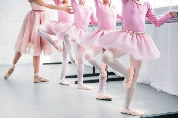 Tiro recortado de crianças em saias tutu rosa praticando balé com professor na escola de balé — Fotografia de Stock