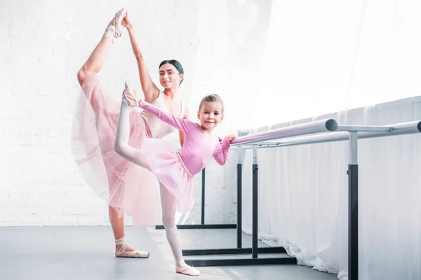 Hermosas bailarinas adultas y pequeñas que se estiran y sonríen a la cámara en la escuela de ballet - foto de stock