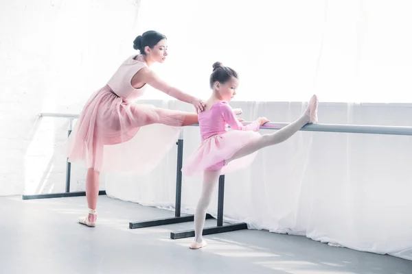 Junge Ballettlehrerin beobachtet kleine Schülerin beim Dehnen im Ballettstudio — Stockfoto