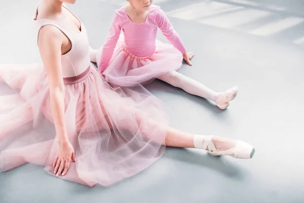 Recortado tiro de profesor de ballet y poco estudiante estirándose juntos en estudio de ballet - foto de stock