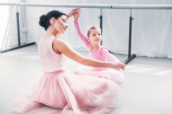 Lächelnde junge Ballettlehrerin und kleine Schülerin in rosa Tutu-Röcken beim gemeinsamen Training in der Ballettschule — Stockfoto