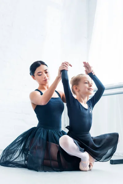 Beautiful young ballet teacher training adorable flexible kid in ballet school — Stock Photo