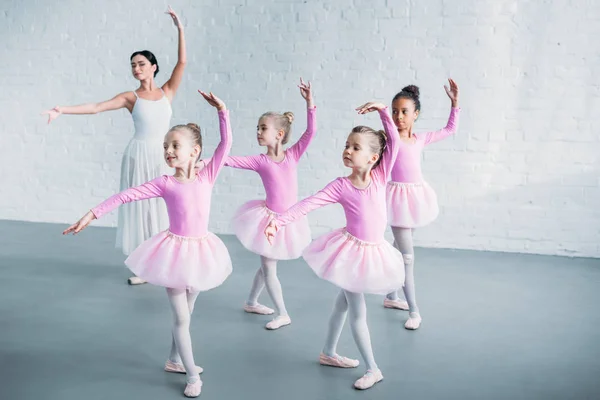 Adorable kids in pink tutu skirts practicing ballet with young teacher in ballet school — Stock Photo