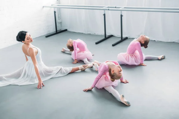 Adorables bailarinas y maestras jóvenes estirándose y ejercitándose juntas en la escuela de ballet - foto de stock