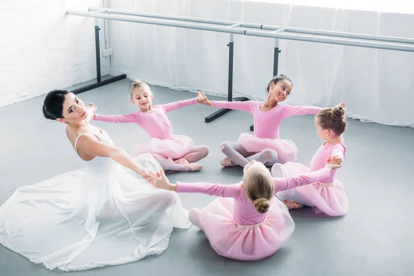 Adorables pequeñas bailarinas y jóvenes maestras practicando juntas en la escuela de ballet - foto de stock