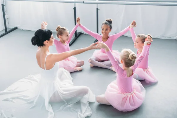 Joyeuses petites ballerines et professeur de ballet assis et tenant la main à l'école de ballet — Photo de stock